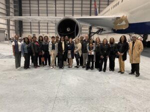 Industry tour group stands in front of plane that is being painted.