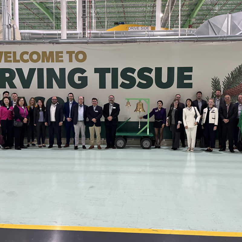 A group of international representative pose in front of a mural that reads "Welcome to Irving Tissue."